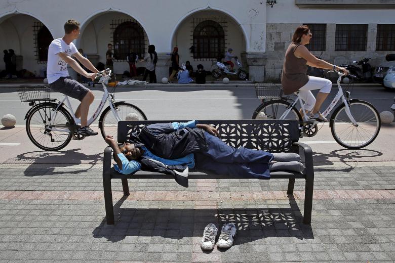An-Afghan-immigrant-sleeps-on-a-bench-outside-a-local-police-station-as-tourists.jpg